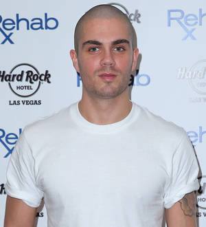Max George in a black suit with a white shirt and tie posing on a red carpet
