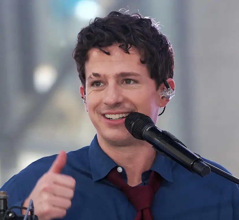 Stephen Puth sits on a bar stool, smiling, with a guitar leaning on him, in a behind-the-scenes shot